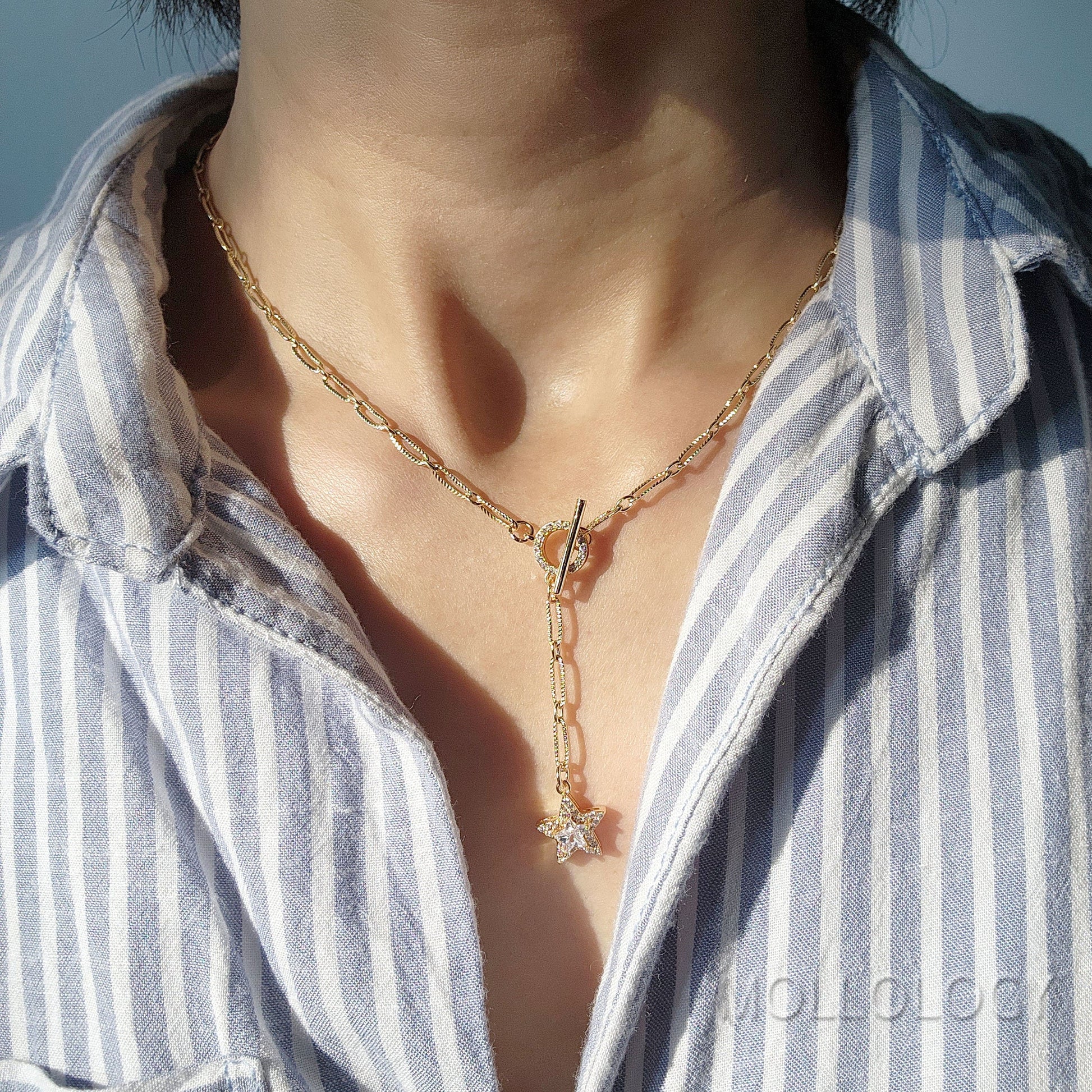 A person wearing a gold chain link necklace with a star charm, layered over a striped shirt.