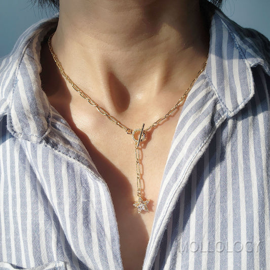 A person wearing a gold chain link necklace with a star charm, layered over a striped shirt.