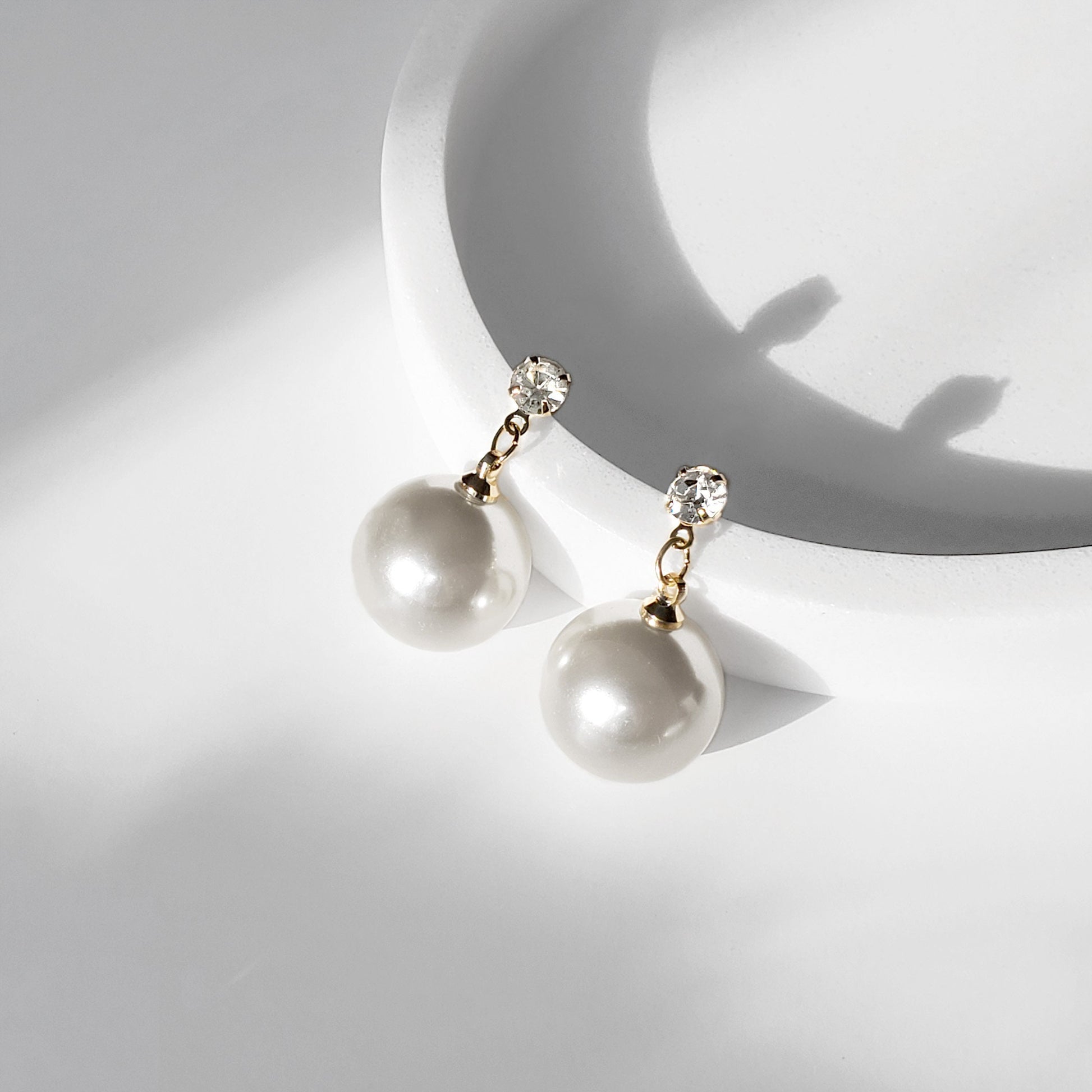 A pair of pearl drop earrings with gold-plated brass bands and round cubic zirconia studs, displayed on a white stand.