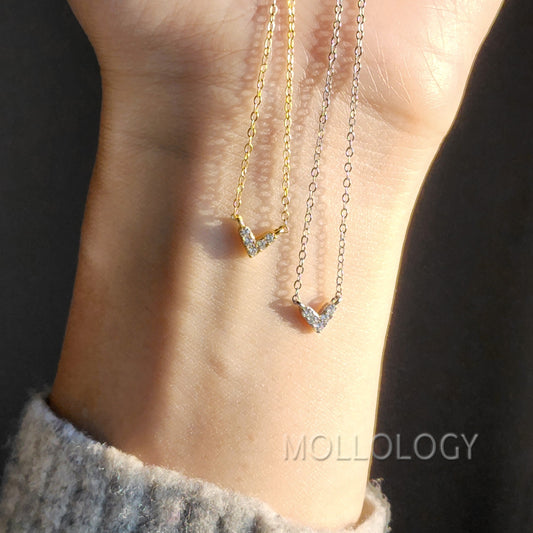 A dainty gold-colored heart-shaped necklace with small cubic zirconia accents, worn on a chain.